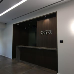 Una recepción con detalles de madera oscura y el texto 'BOUTIQUE HOTEL ADELAR' en la pared.