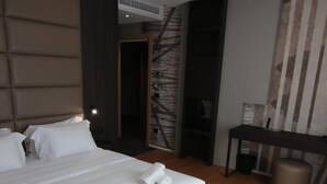Ett modernt hotellrum med en stor säng, ett skrivbord och utsikt över en byggnad utanför.