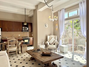 A modern kitchen with wooden cabinets, a dining area with a wooden table, and a view of a garden through large sliding doors. - by Calamari.Homes - Centenario 304 - Old City (Cartagena de Indias)
