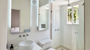 Un baño moderno con un espejo grande, dos lavamanos, un inodoro y una cabina de ducha de vidrio.