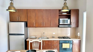 Cocina compacta con armarios de madera, refrigerador de acero inoxidable, microondas, estufa a gas y lavavajillas.