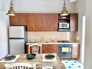 A compact kitchen with wooden cabinets, a stainless steel refrigerator, a microwave, a gas stove, and a dishwasher. - by Calamari.Homes - Centenario 304 - Old City (Cartagena de Indias)