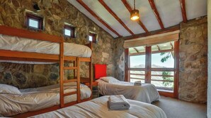 Una stanza con letti a castello, pareti in pietra, travi in legno, una sedia rossa e una finestra vista.