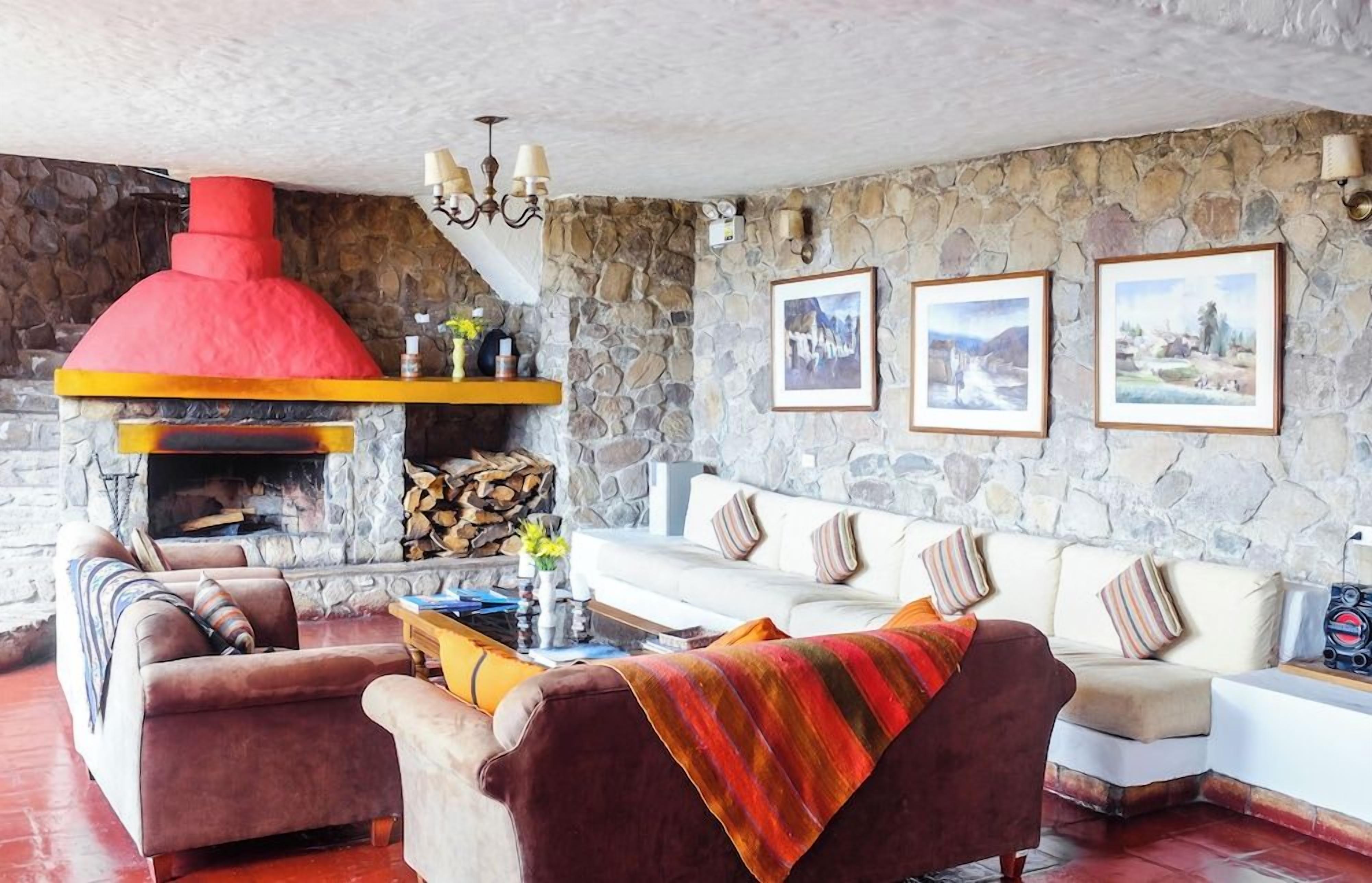 Una sala de estar acogedora con una pared de piedra, una chimenea roja, un conjunto de sofás blancos y cuadros enmarcados.