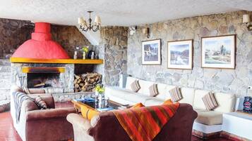 Una sala de estar acogedora con una pared de piedra, una chimenea roja, un conjunto de sofás blancos y cuadros enmarcados.