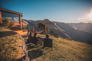 A group of people relaxing on a grassy hill with a view of mountains, a hammock, and a glass building.