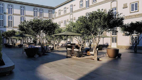 Un patio exterior con zonas de estar, sombrillas y árboles.