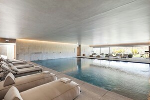 Una piscina interior moderna con sillones de descanso y una zona de hamacas.