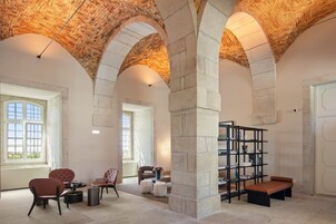 Una habitación amplia con techos abovedados, una zona de estar con sillas y un banco, y una estantería.