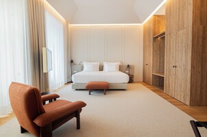 Un dormitorio moderno con una cama grande, un armario de madera, una zona de estar y una mesita de noche.
