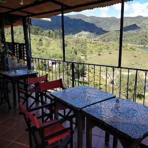 A terrace with tiled tables and chairs, overlooking a mountainous landscape with a river. - Casa Encuentro Ecolodge (Guatapé)