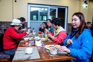 Un grupo de personas cenando en un restaurante con una pared de ladrillo y una ventana al fondo.