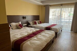 Habitación de hotel con dos camas, cabecero de madera, ventana con cortinas y suelo de madera.