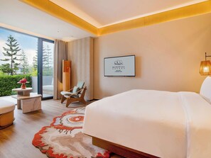 Habitación de hotel con una cama grande, una silla, una mesita con fruta y vistas a los árboles por la ventana.