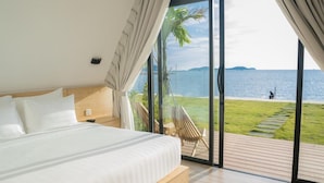 A bedroom with a large bed, a view of the sea, and a deck with a chair. - Summer Bay Beach Club and Cabins Sihanoukville by Preference (Prey Nob)