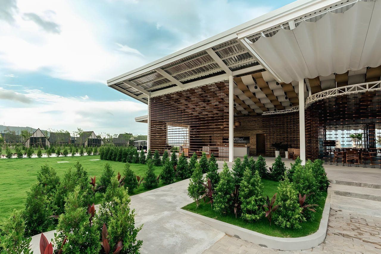 Een modern gebouw met een overdekt terras, omringd door verzorgde beplanting en een heldere lucht.