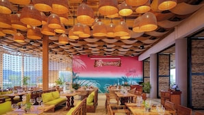 A restaurant with wooden tables and chairs, a mural on the wall, and hanging wicker lamps. - Summer Bay Beach Club and Cabins Sihanoukville by Preference (Prey Nob)