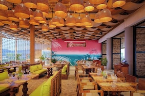 Un restaurante con mesas y sillas de madera, un mural en la pared y lámparas de mimbre colgantes.