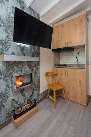 A compact kitchen with a built-in TV, a wood cabinet, a small seating area, and a fireplace. - Hotel Lares 70 (Medellín)