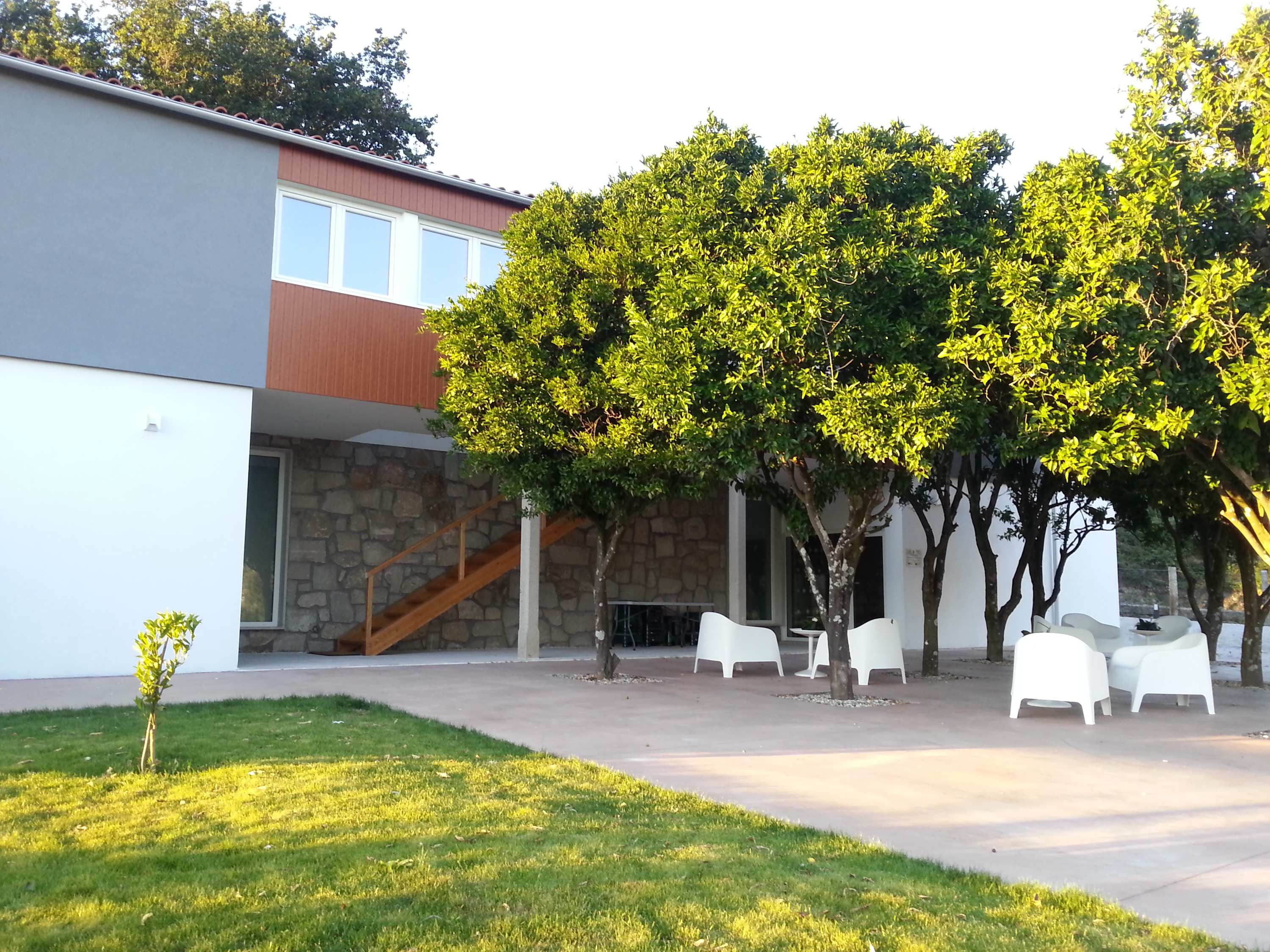Un edificio con fachada de piedra, una escalera y un área de estar al aire libre con sillas blancas.