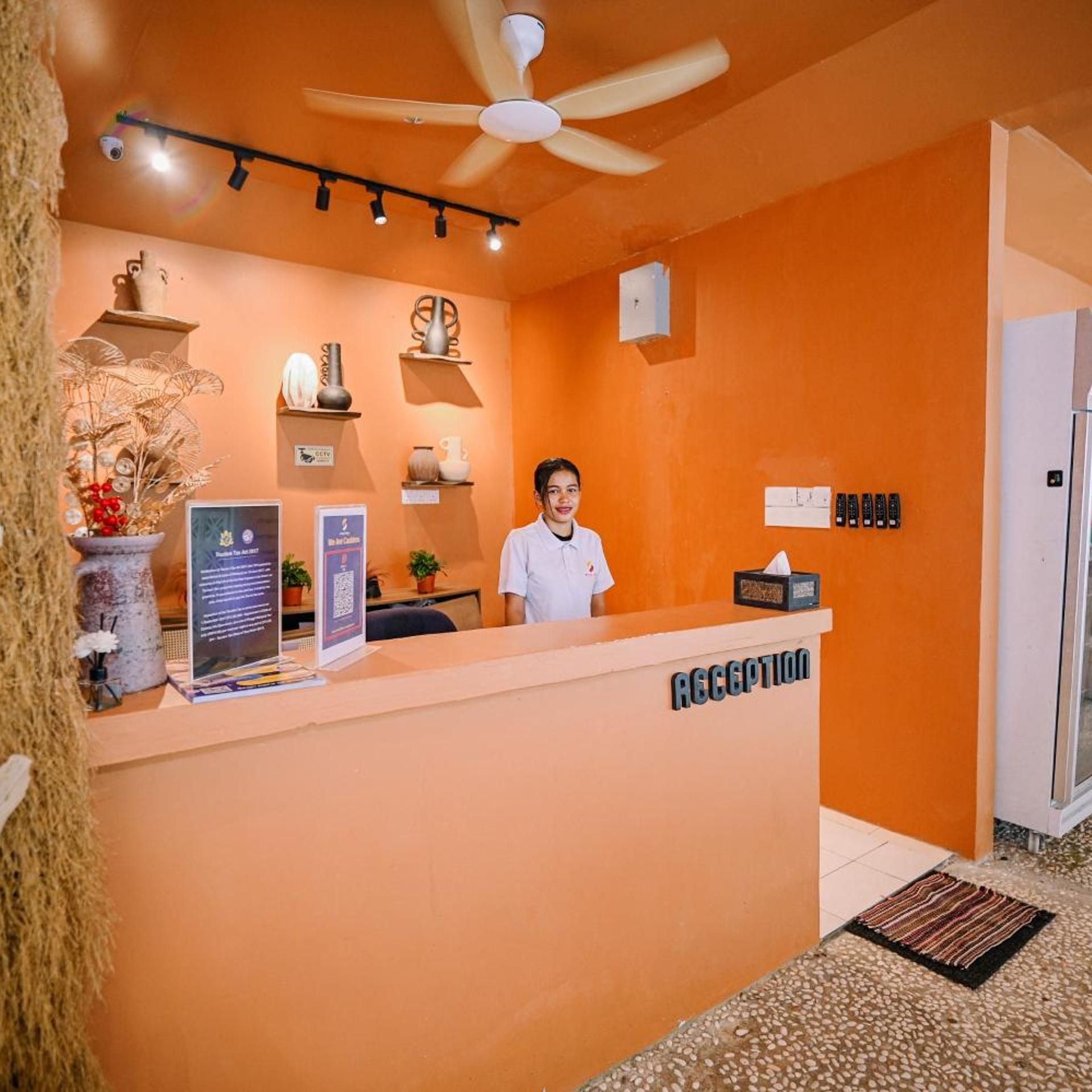 A reception area with a receptionist, a ceiling fan, a wall-mounted CCTV camera, and a sign indicating the reception desk.
