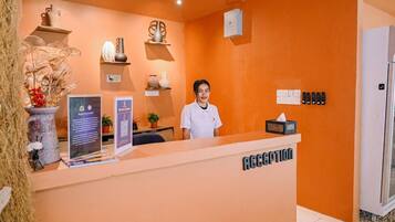 A reception area with a receptionist, a ceiling fan, a wall-mounted CCTV camera, and a sign indicating the reception desk.