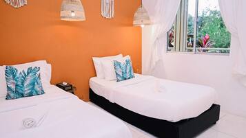 A room with two beds, a window with curtains, and macrame wall hangings.