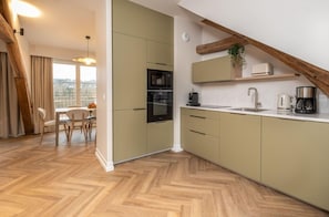 A modern kitchen with built-in appliances, a dining area with a table and chairs, and a view through a window. - L'horloge (Montevrain)