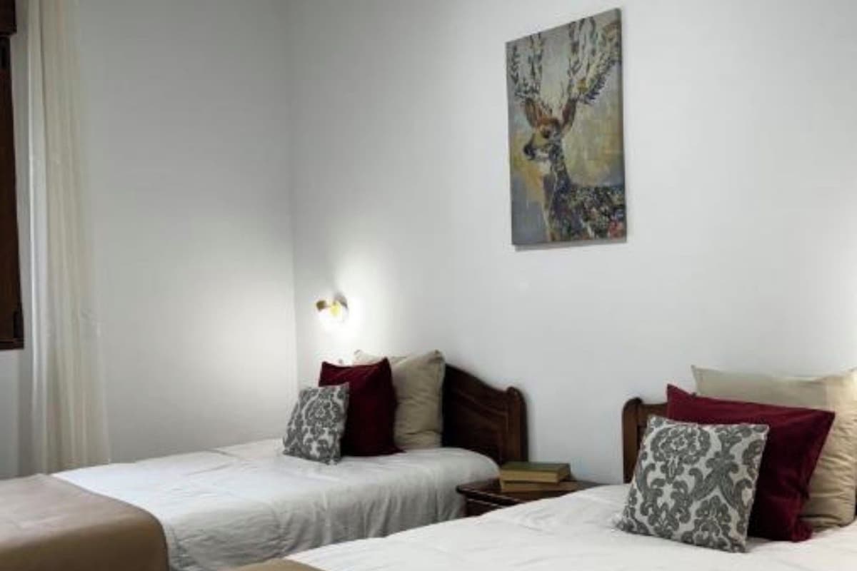 A hotel room with two single beds, a nightstand, a wall-mounted lamp, and a painting.