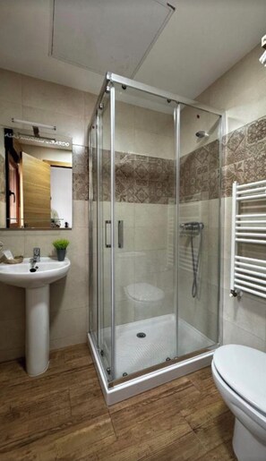 A bathroom with a glass-enclosed shower, a sink, and a toilet.