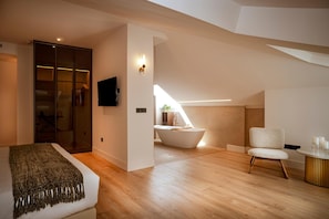 A modern bedroom with a large bed, a TV, a walk-in closet, and a bathroom with a bathtub. - Hotel Cigarral Santa Maria (Toledo)