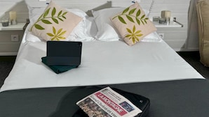 A hotel room with a bed, pillows, a bedside table, a lamp, a phone, and a newspaper. - Hotel De La Tour Saint Etienne SUD (Saint-Etienne)