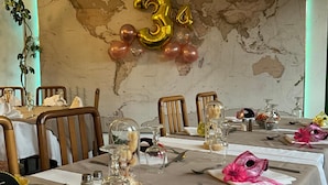 A dining area with tables set for a celebration, featuring a world map backdrop and balloons. - Hotel De La Tour Saint Etienne SUD (Saint-Etienne)