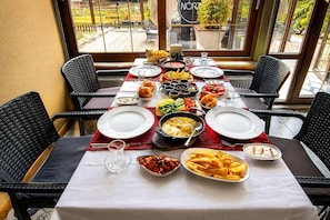 A dining table set with various dishes, surrounded by wicker chairs, in a room with large windows. - 216 North Hotel - Agva (Şile)