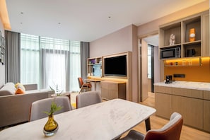 A modern hotel room with a dining area, a flat-screen TV, a kitchen with a microwave, and a large window with curtains. - Home2 Suites by Hilton Guangzhou Huadu (Guangzhou)