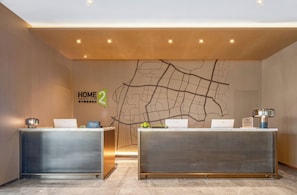 Una recepción de hotel con dos recepcionistas, un mapa en la pared y un cartel que indica 'HOME 2' y 'Hilton Honors'.