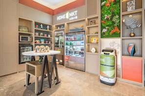 A modern interior with a central round table, a refrigerator stocked with beverages, and a vending machine. - Home2 Suites by Hilton Guangzhou Huadu (Guangzhou)