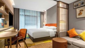 Una habitación de hotel con cama, escritorio, silla, sofá y un pequeño taburete redondo.