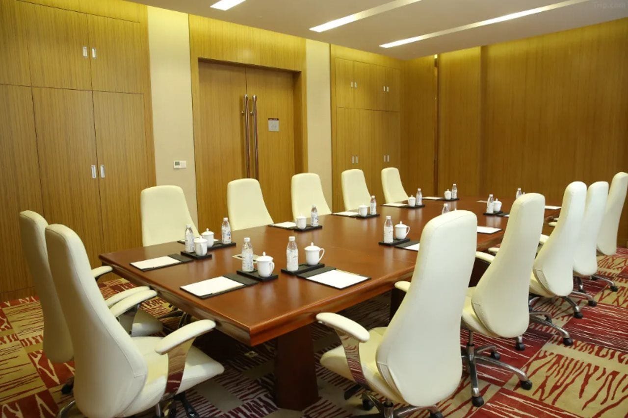 A conference room with a long table, white chairs, and a carpeted floor.