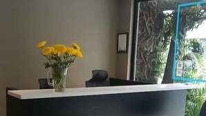 En receptionsdisk med en vas med gula blommor, en svart stol och utsikt över grönområden utanför.