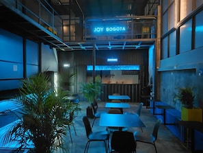 Un interior moderno con zona de restaurante, diferentes disposiciones de asientos y un letrero visible que dice 'JOY BOGOTA'.