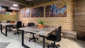 A conference room with four tables, each with two chairs, and a brick wall with four paintings. - Inactivo Hotel Natura Express (Medellín)