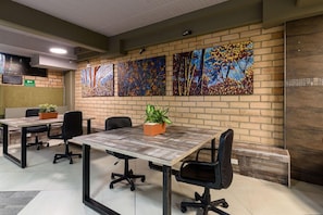 A conference room with four tables, each with two chairs, and a brick wall with four paintings. - Inactivo Hotel Natura Express (Medellín)