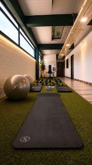 A gym with exercise equipment, a yoga mat, and a wall-mounted dumbbell rack. - Inactivo Hotel Natura Express (Medellín)