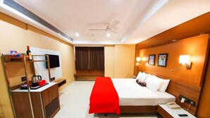 Habitación de hotel con cama, mesita de noche, escritorio con silla, televisor y una manta roja.
