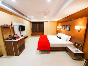 Ein Hotelzimmer mit Bett, Nachttisch, Schreibtisch mit Stuhl, Fernseher und roter Tagesdecke.