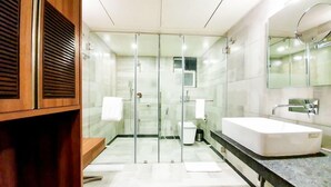 Un baño moderno con cabina de ducha de vidrio, un lavabo grande blanco y un mueble de tocador de madera.