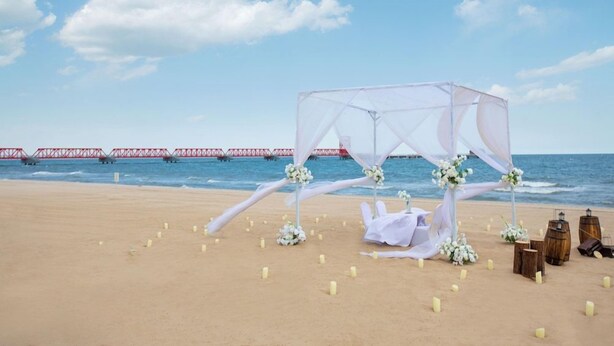 Hochzeitsdekoration am Strand mit einer Markise, Blumenschmuck und einer Holzbank.