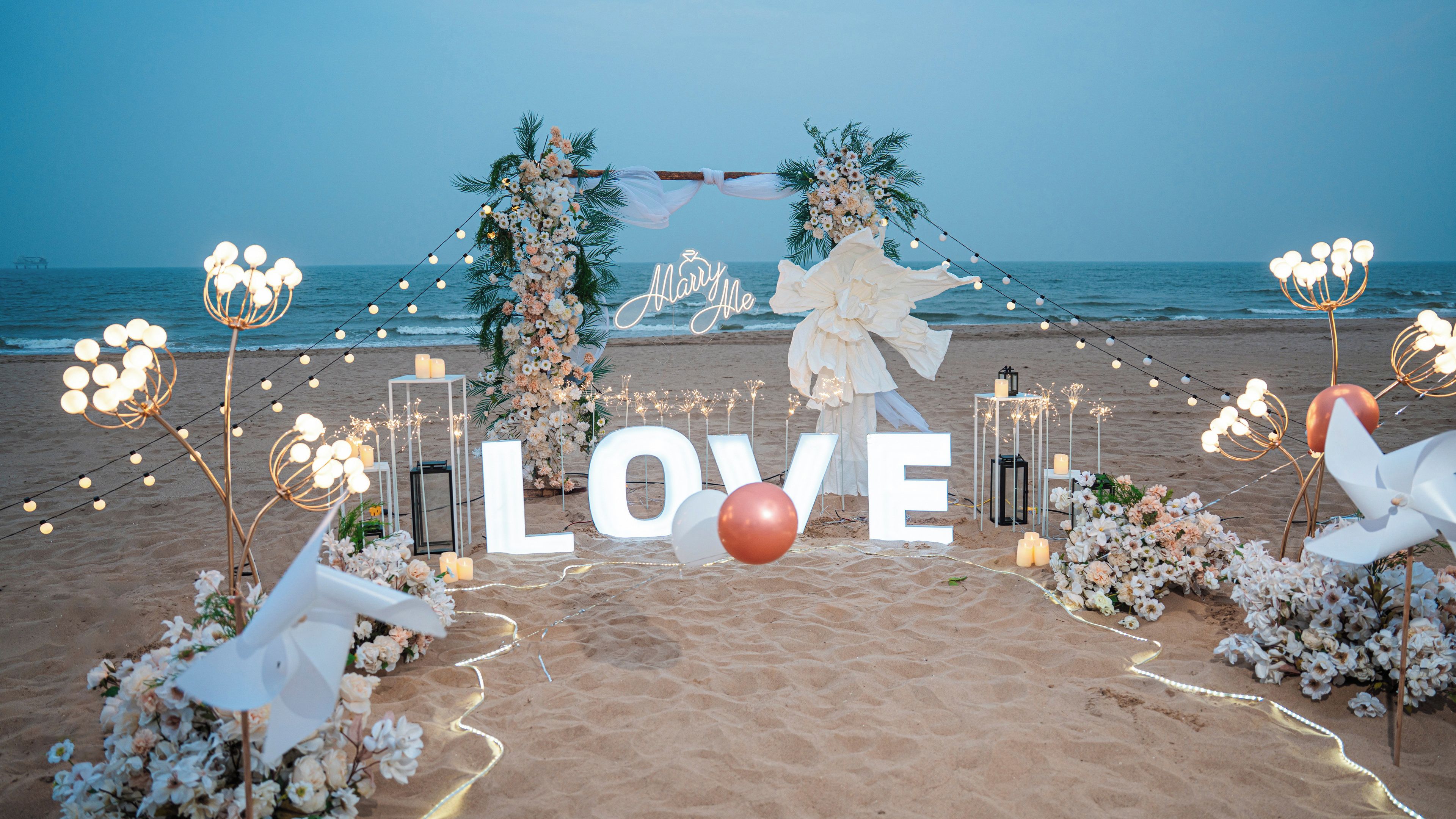 A beach wedding setup with a floral arch and the word "LOVE" in large letters.