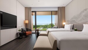 Ein Hotelzimmer mit großem Fernseher, zwei Betten, einem Schreibtisch und Blick auf einen Fluss.